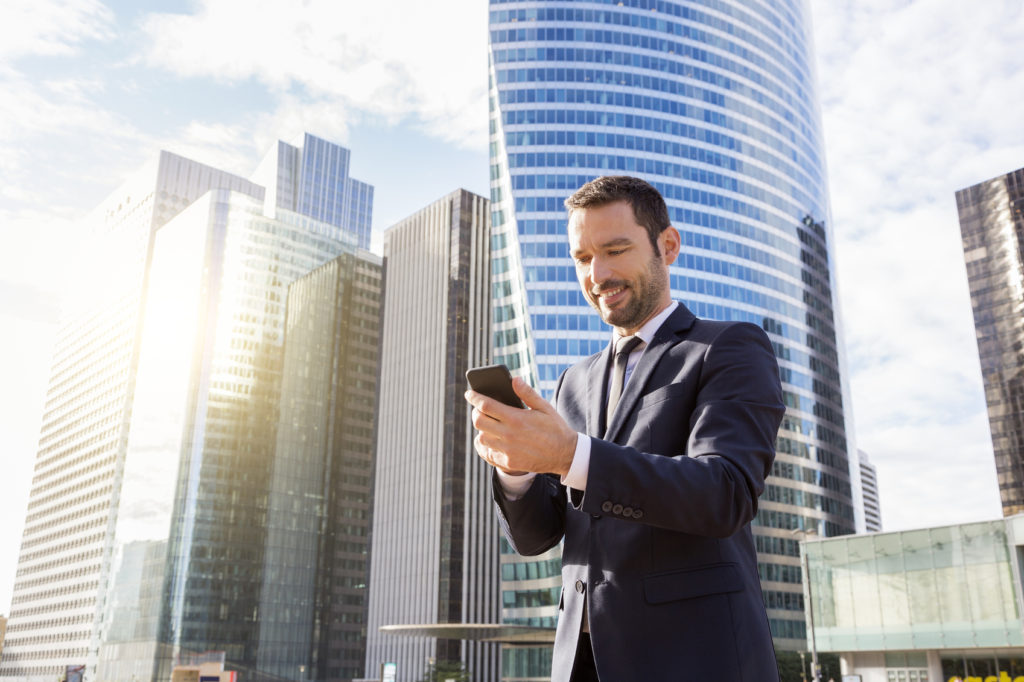 Business professional using a smartphone outside a high-rise building, symbolizing the evolving short-term rental market in Australia.